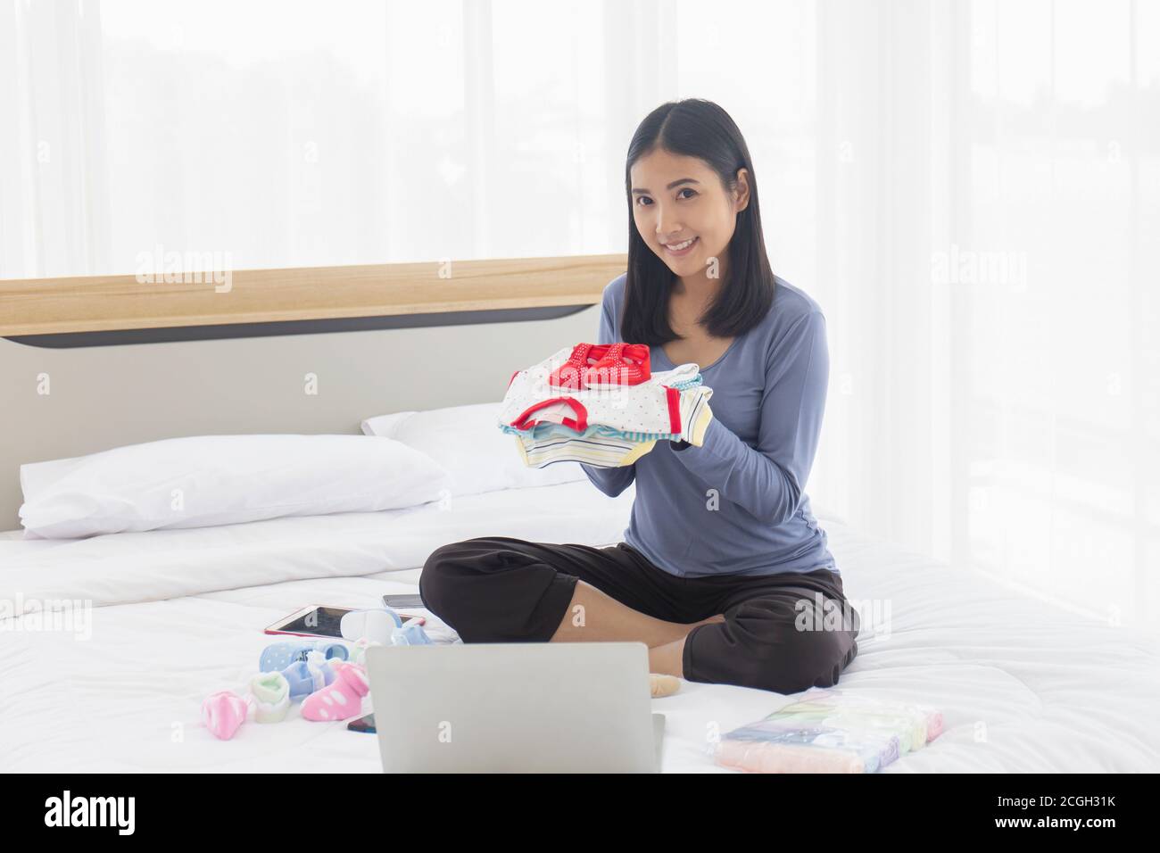 Une mère asiatique choisit des vêtements pour son bébé au lit avec un sourire éclatant. Banque D'Images