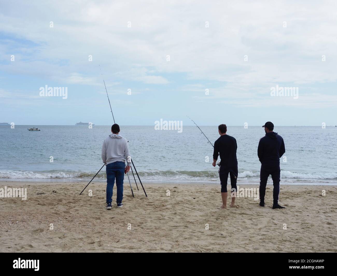 trois hommes pêchant dans la mer depuis une plage vue de l'arrière Banque D'Images