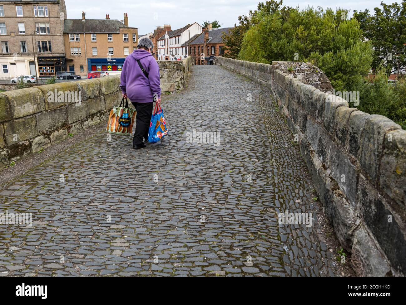 Femme transportant des sacs d'épicerie marchant sur le vieux pont romain pavé, Musselburgh, East Lothian, Écosse, Royaume-Uni Banque D'Images