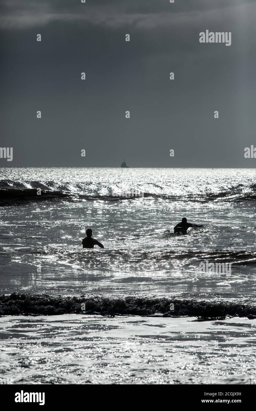 Le surfeur silhouetté se promène dans les petites vagues à côté de la jetée de la plage de Bournemouth pour profiter du soleil d'hiver et surfer avant le début de la pluie. Banque D'Images
