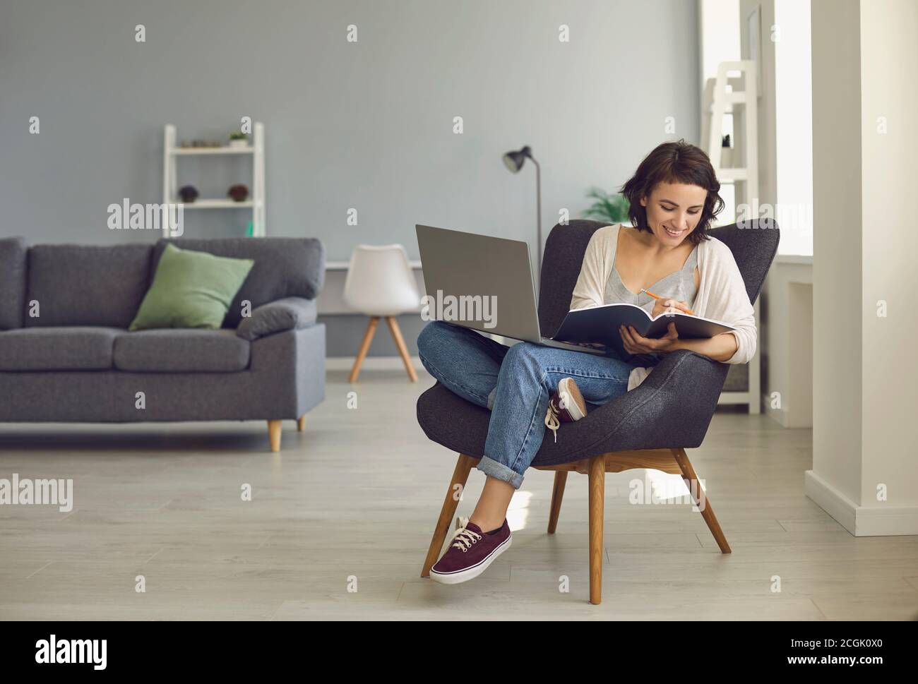 Femme souriante assise à la maison avec un ordinateur portable et prenant des notes pendant la leçon en ligne Banque D'Images
