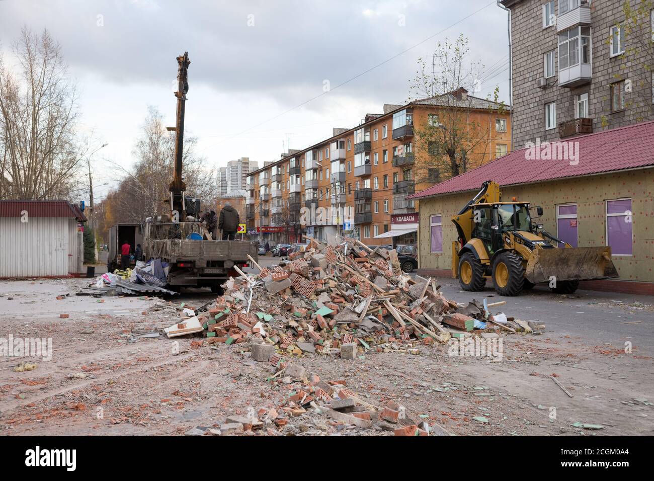 Une pile de déchets de démolition d'anciens pavillons se trouve dans la rue de la ville, près du bulldozer et du camion, pendant le processus de travail en automne. Banque D'Images