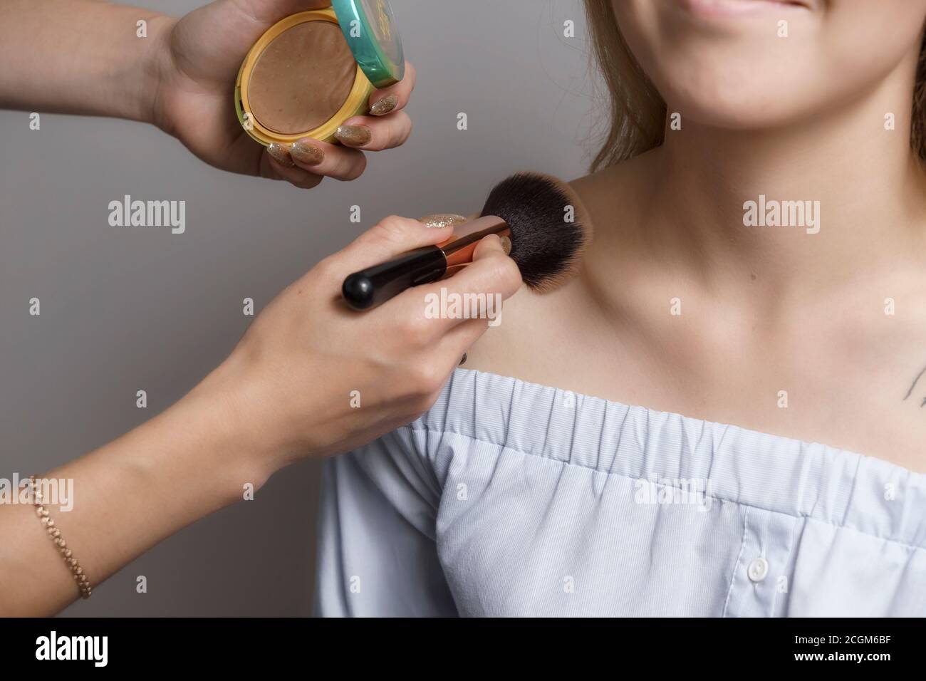 Le maquilleur applique de la poudre sur la poitrine et les épaules du mannequin. Concentrez-vous sur le pinceau à maquillage. Processus de maquillage professionnel Banque D'Images