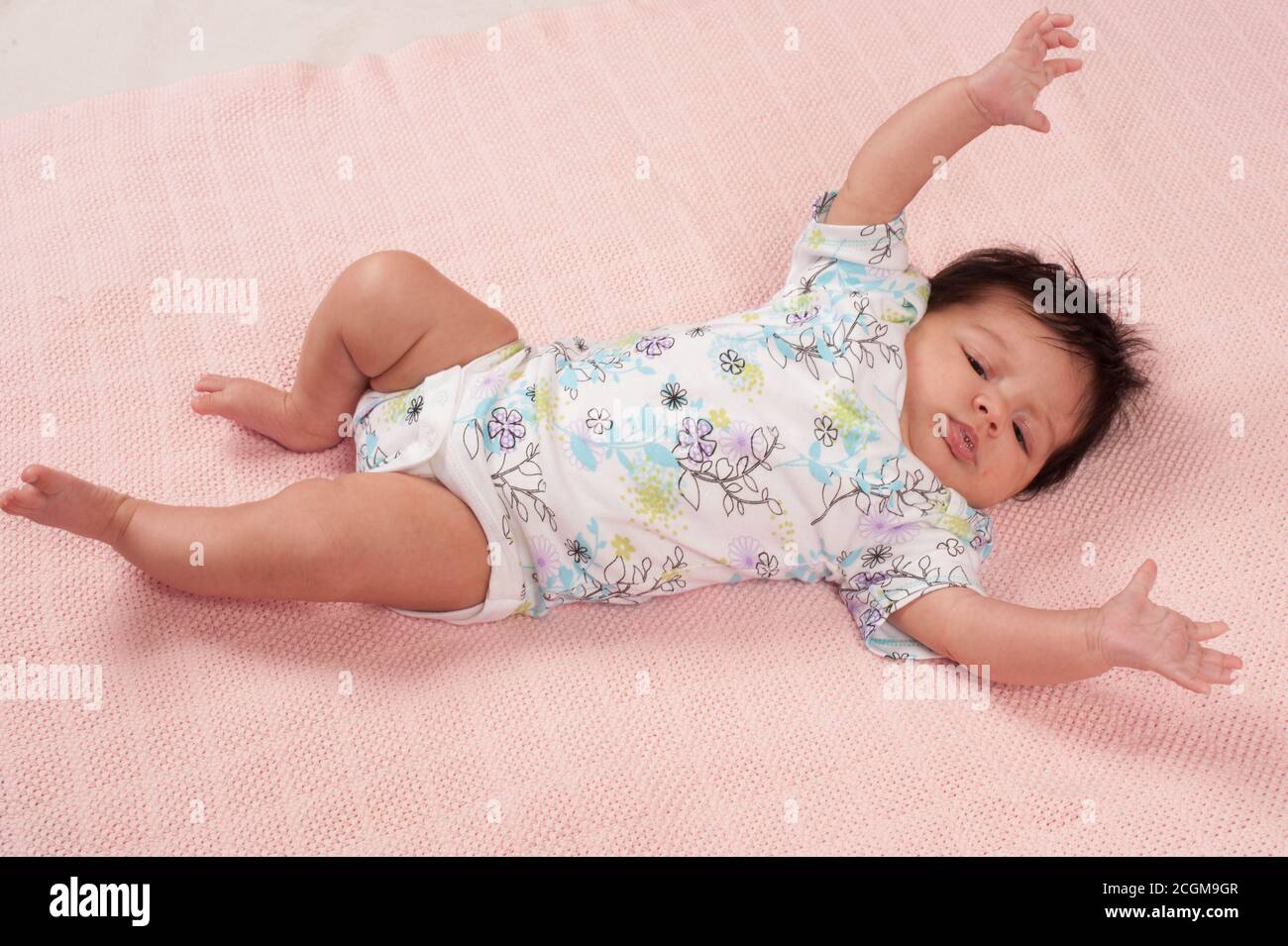 Nouveau-né bébé fille un mois Startle Reflex (Moro Reflex) horizontal allongé sur toute la longueur sur une couverture rose Banque D'Images