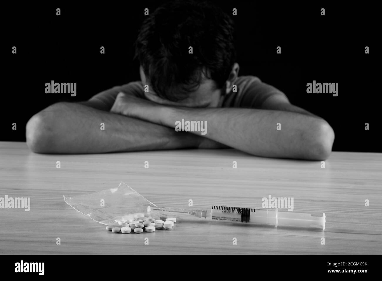 Homme addict de drogue assis avec la seringue et les drogues hors de mise au point en arrière-plan, photo en noir et blanc Banque D'Images