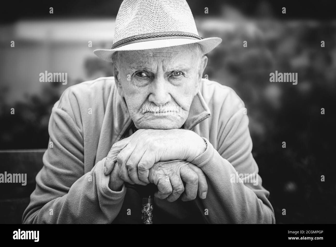 triste, fâché vieil homme dans un chapeau est assis dans un jardin en plein air. le concept de solitude et de vieux âge solitaire. Portrait en noir et blanc Banque D'Images