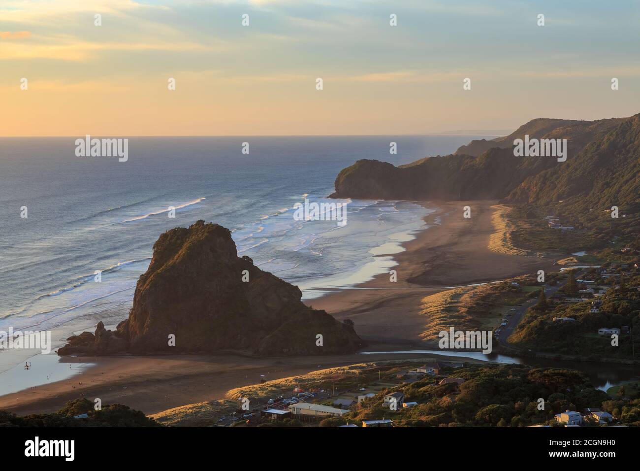 Piha, Nouvelle-Zélande, au coucher du soleil. Lion Rock surplombe la plage de sable noir. En arrière-plan se trouve te Waha point Banque D'Images