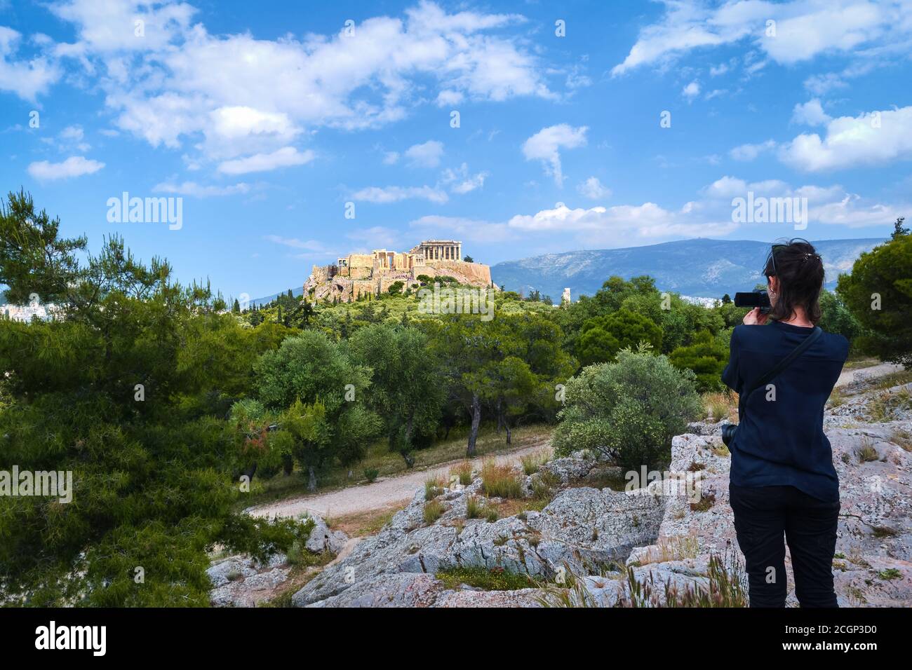 Une touriste femelle non reconnaissable vêtue de noir prend une vue sur l'Acropole et la colline de Lycabette à Athènes, Grèce de la colline de Pnyx le jour d'été ensoleillé Banque D'Images