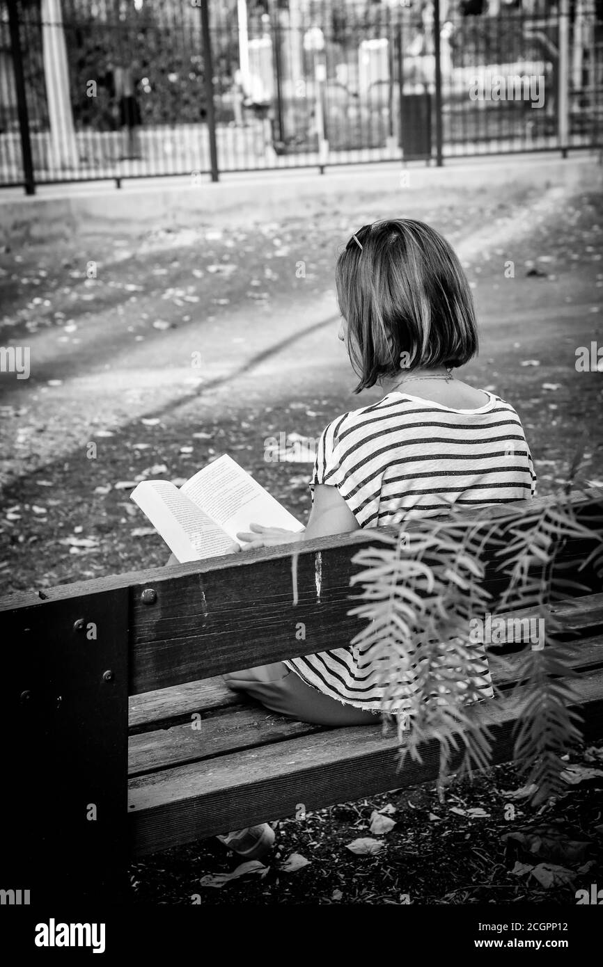 Femme seule lisant un livre dans un parc, assise sur un banc Banque D'Images