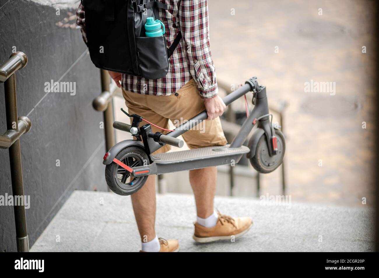 Le jeune homme caucasien en vêtements décontractés avec un sac à dos porte  un scooter électrique plié dans sa main jusqu'à l'escalier d'un immeuble de  bureau. Homme transportant Photo Stock - Alamy