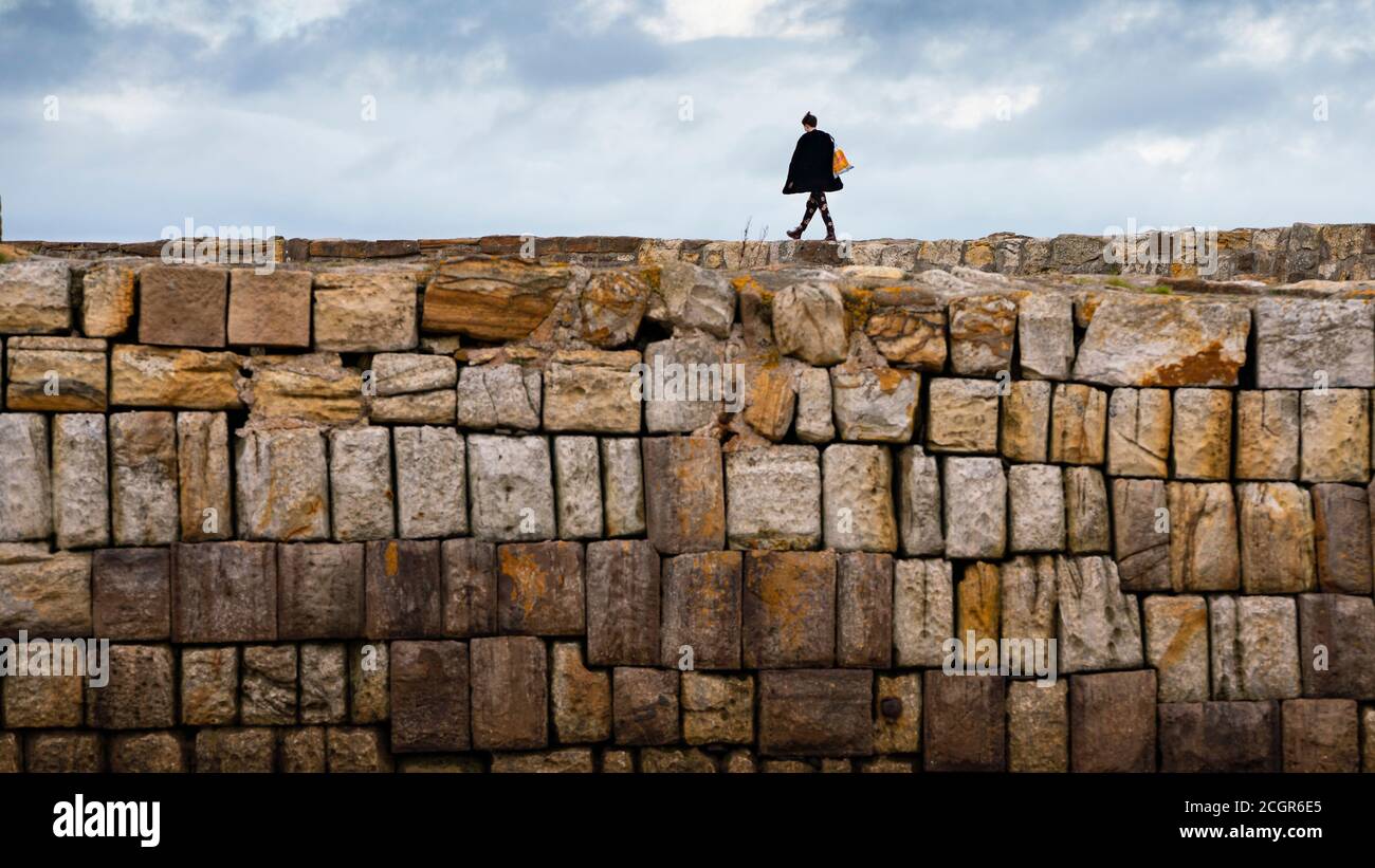 Femme solitaire marchant sur le mur du port à St Andrews, Fife, Écosse, Royaume-Uni Banque D'Images
