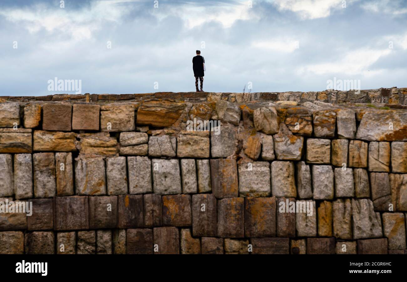 Femme solitaire debout sur le mur du port à St Andrews, Fife, Écosse, Royaume-Uni Banque D'Images