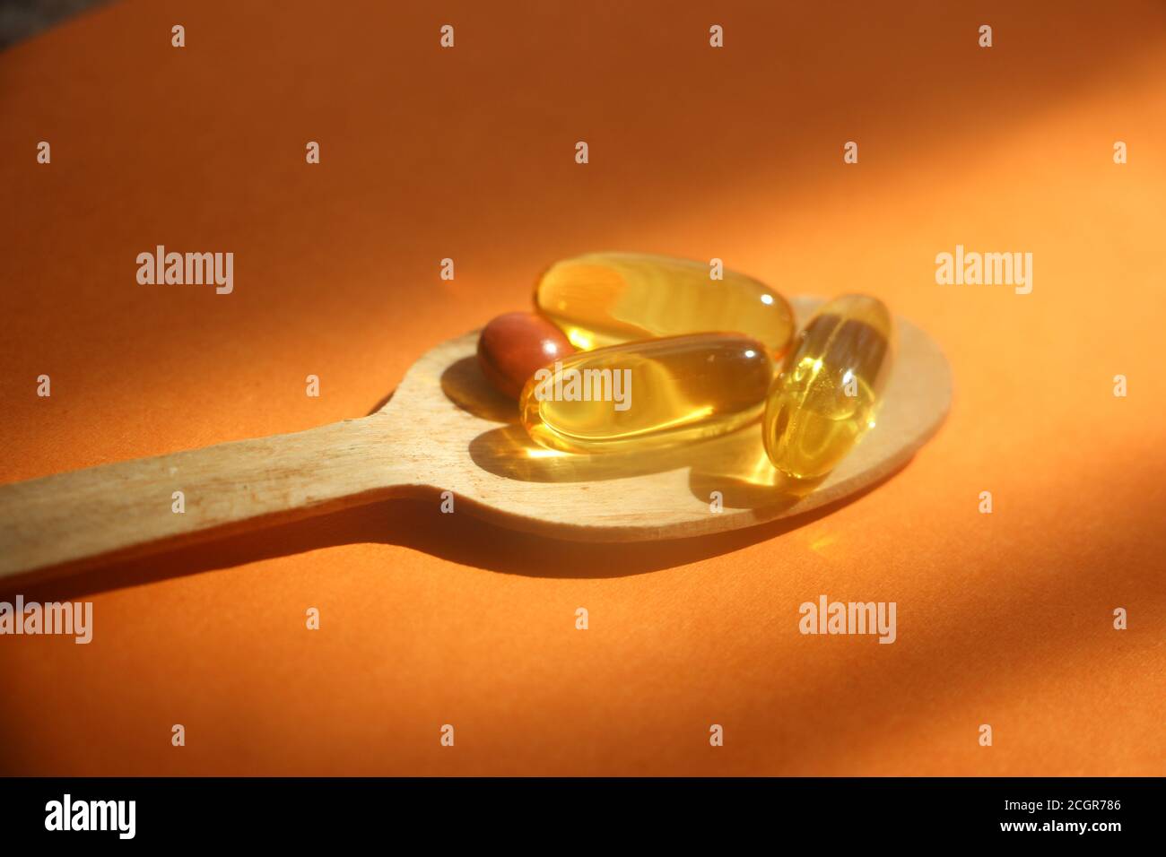 capsules de gel oméga d'huile de foie de morue dans une cuillère en bois sur fond orange. Concept de soins de santé Banque D'Images