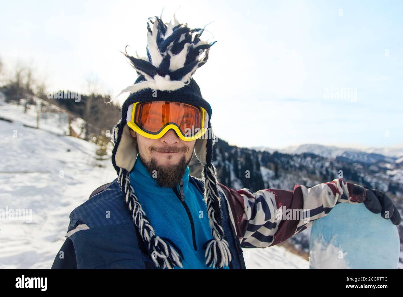Drôle de barbu homme Snowboarder portrait en chapeau mohawk aime le station de ski dans les montagnes Banque D'Images