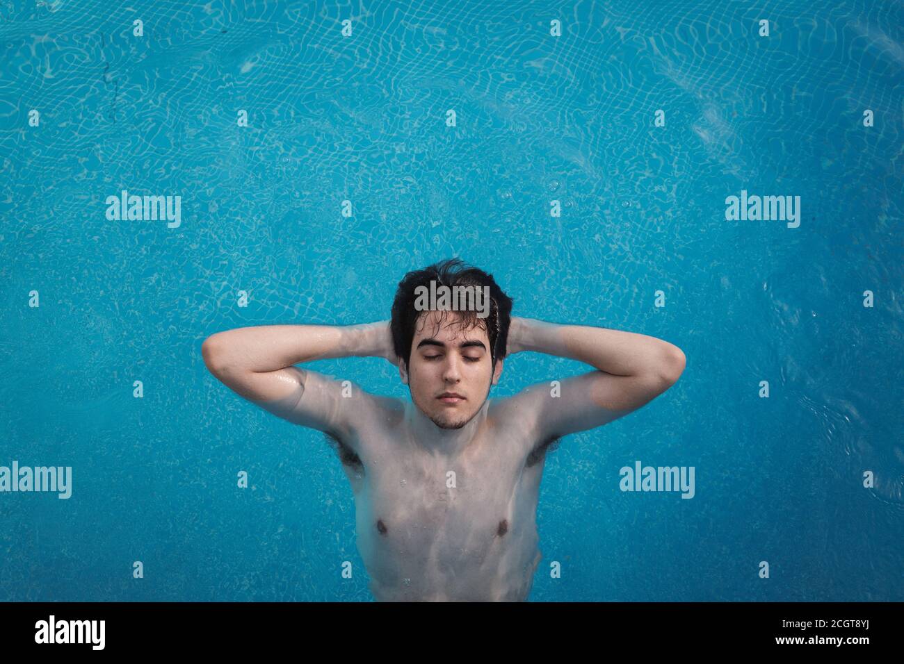 Vue de dessus d'un jeune homme avec ses yeux fermés, flottant dans une piscine avec ses mains à l'arrière de sa tête. Profiter de vacances tout en prenant un bain de soleil Banque D'Images