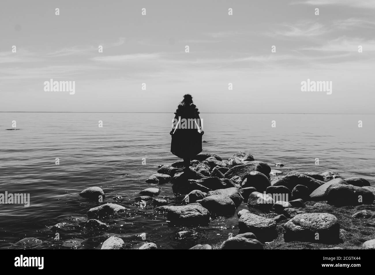 Silhouette d'une femme debout sur des pierres à la plage. Magnifique paysage d'été avec ligne d'horizon. Noir et blanc Banque D'Images