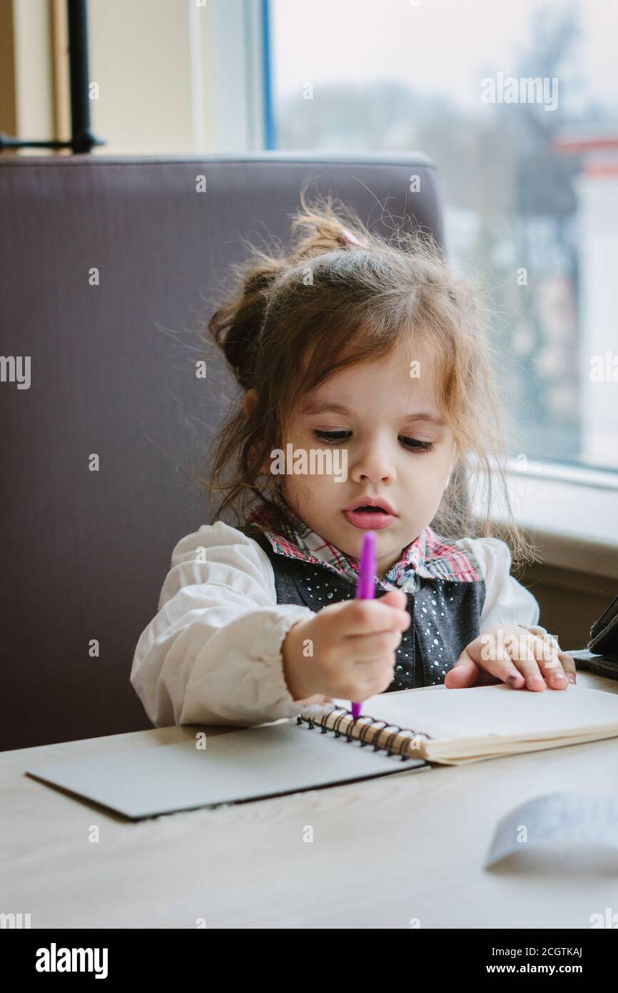 Petite fille d'écriture ou de dessin avec un stylo dans un livre de gravure. Banque D'Images