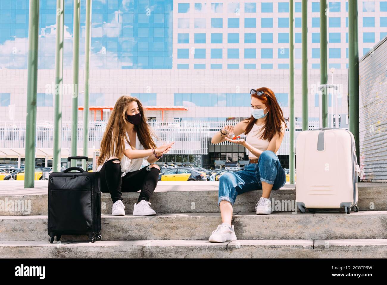 deux jeunes touristes portant un masque facial assis dans un coffre-fort distance en raison de covid-19 utiliser le gel antibactérien pour nettoyer leur mains Banque D'Images deux jeunes touristes portant un masque facial assis dans un coffre-fort distance en raison de covid-19 utiliser le gel antibactérien pour nettoyer leur mains Banque D'Images