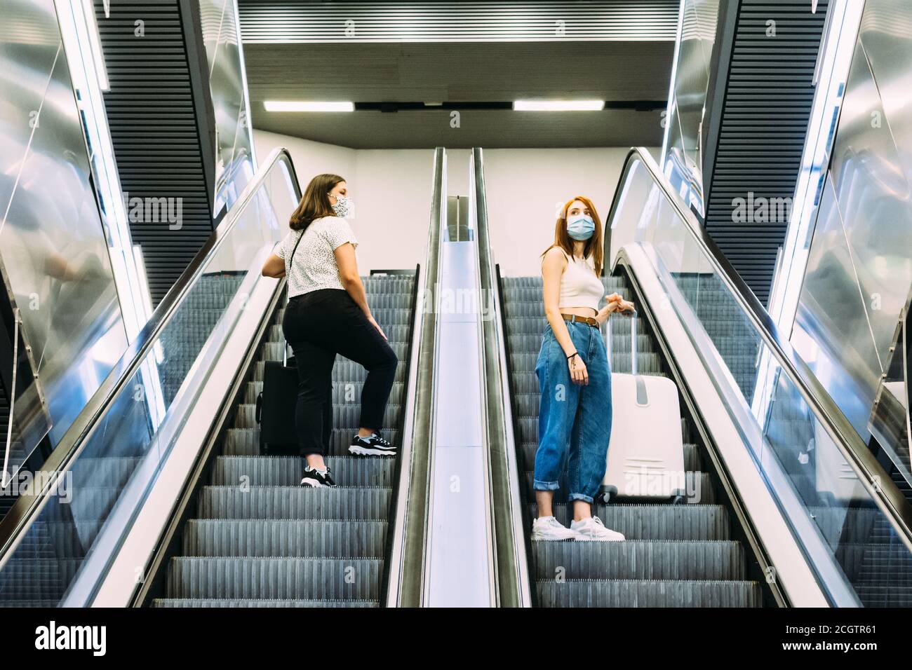 deux jeunes touristes portant un masque utilisent les escaliers mécaniques du métro Banque D'Images