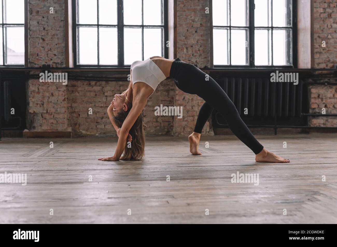 Une jeune femme fait un complexe d'asanas de yoga étirant en classe de style loft. Camatkarasana, Wild Thing, Flip-the-Dog pose. Banque D'Images