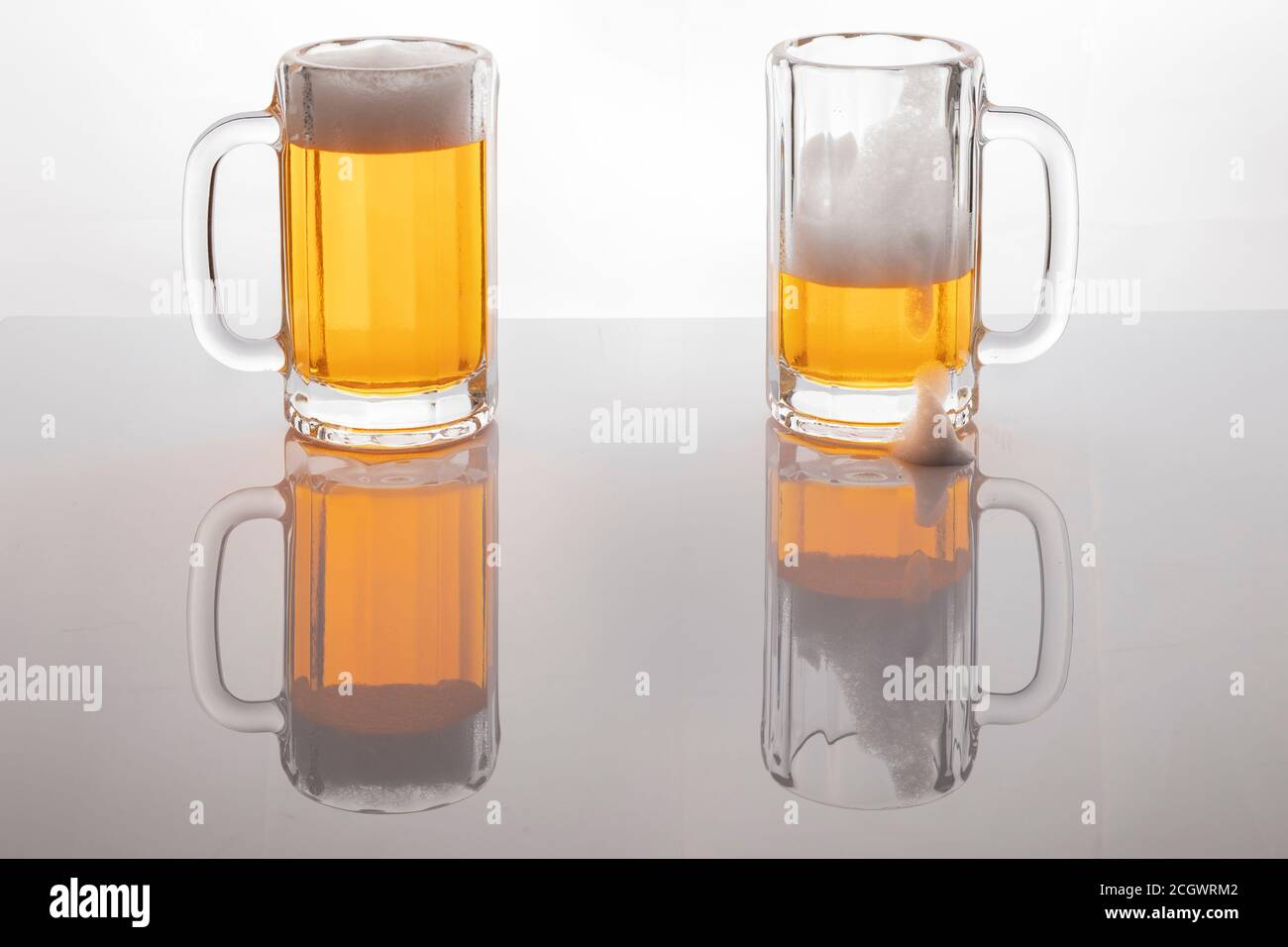 Tasses à bière avec bière. Bière sans glacer. Tasses à bière sur fond blanc rétroéclairé. Un verre presque vide et un plein. Banque D'Images