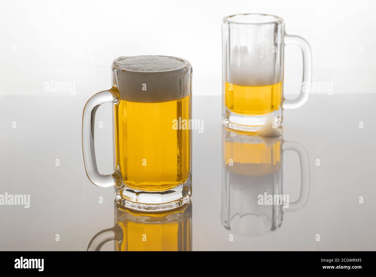 Tasses à bière avec bière. Bière sans glacer. Tasses à bière sur fond blanc rétroéclairé. Un verre presque vide et un plein. Banque D'Images