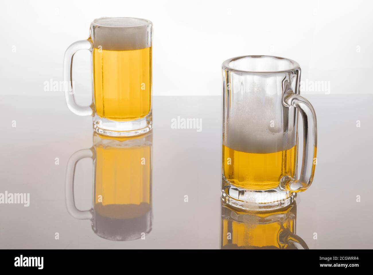Tasses à bière avec bière. Bière sans glacer. Tasses à bière sur fond blanc rétroéclairé. Un verre presque vide et un plein. Banque D'Images