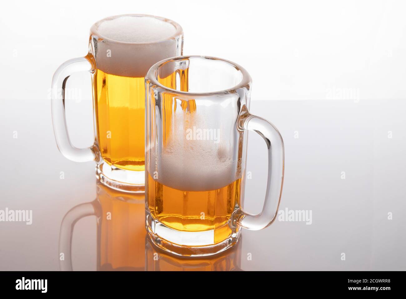 Tasses à bière avec bière. Bière sans glacer. Tasses à bière sur fond blanc rétroéclairé. Un verre presque vide et un plein. Banque D'Images