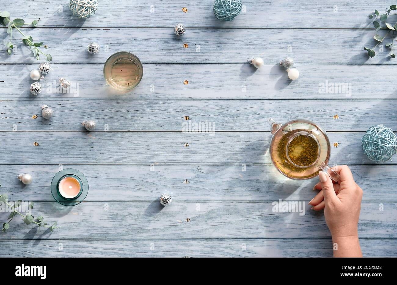 Thé d'hiver, plat avec théière en verre, verre de thé à la main sur des planches en bois bleu pâle. Décorations de Noël sur la table - miroir Banque D'Images