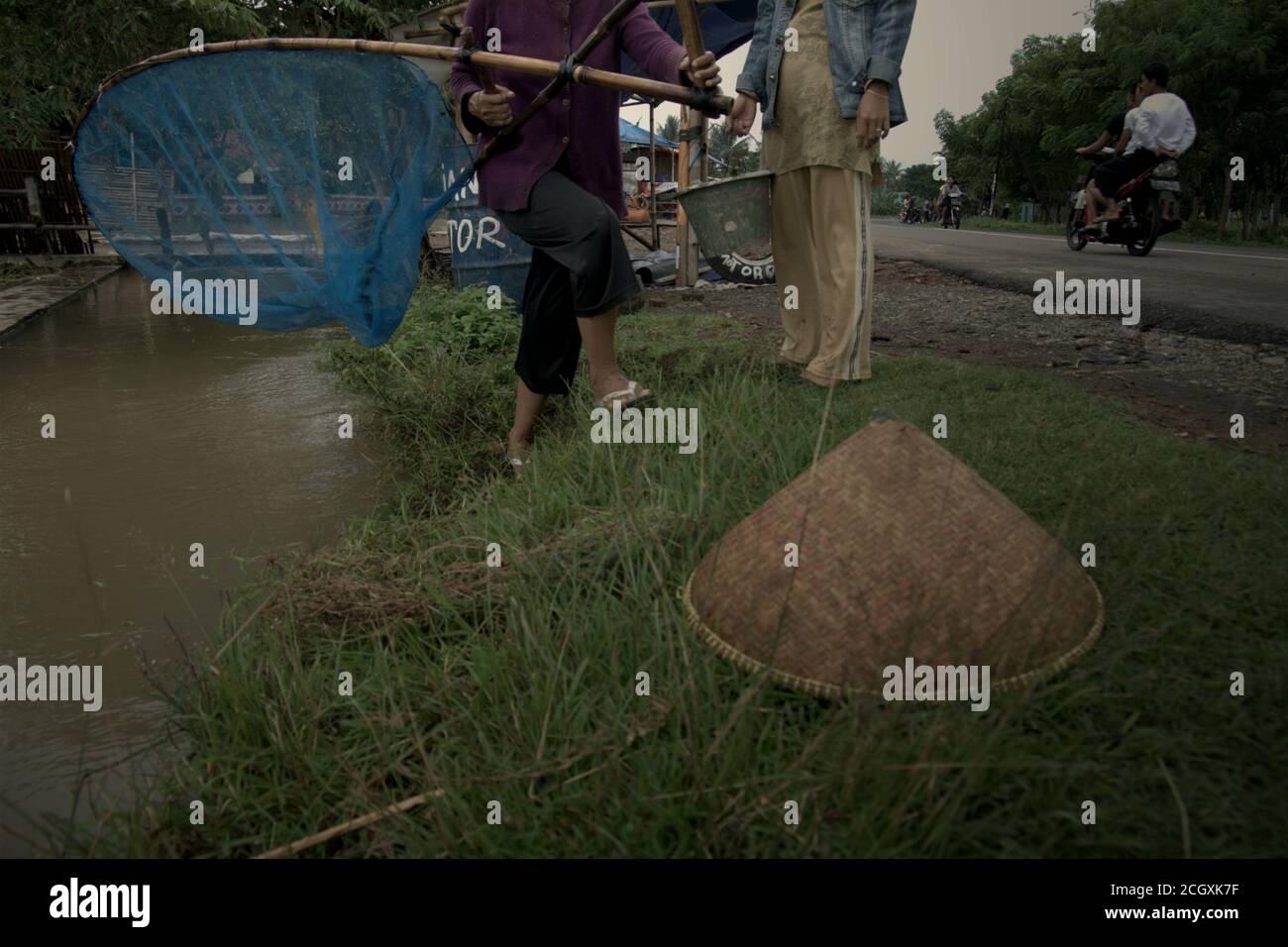 Une femme qui manipule une chathnet alors qu'elle se déplace sur la rive d'un canal d'irrigation de bord de route à Karawang regency, province de Java Ouest, Indonésie. Banque D'Images