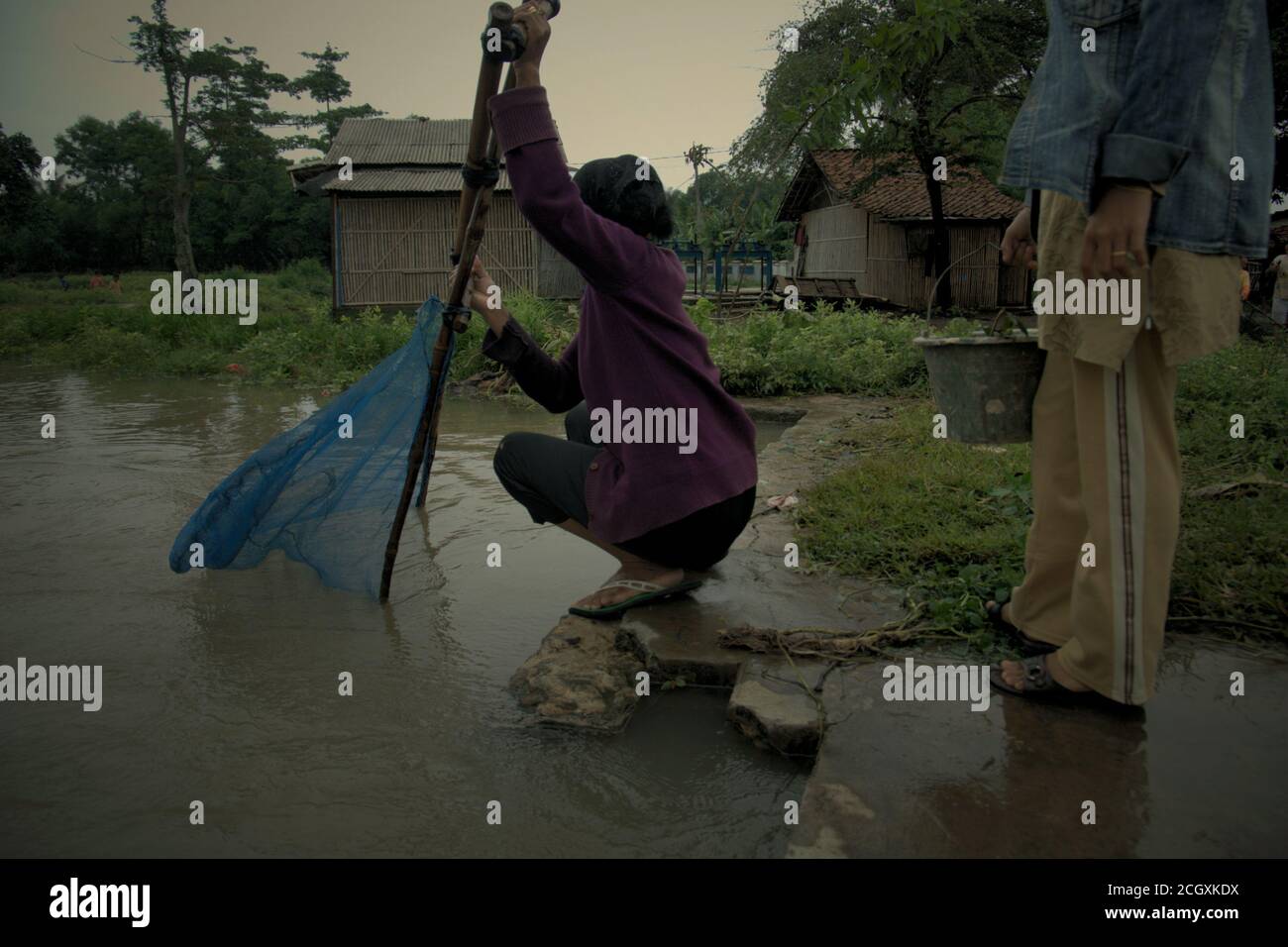 Une femme manipulant le pushnet tandis qu'une amie transportant un seau en plastique contenant des poissons pêchés comme ils pêchent sur un canal d'irrigation à Karawang, Indonésie. Banque D'Images