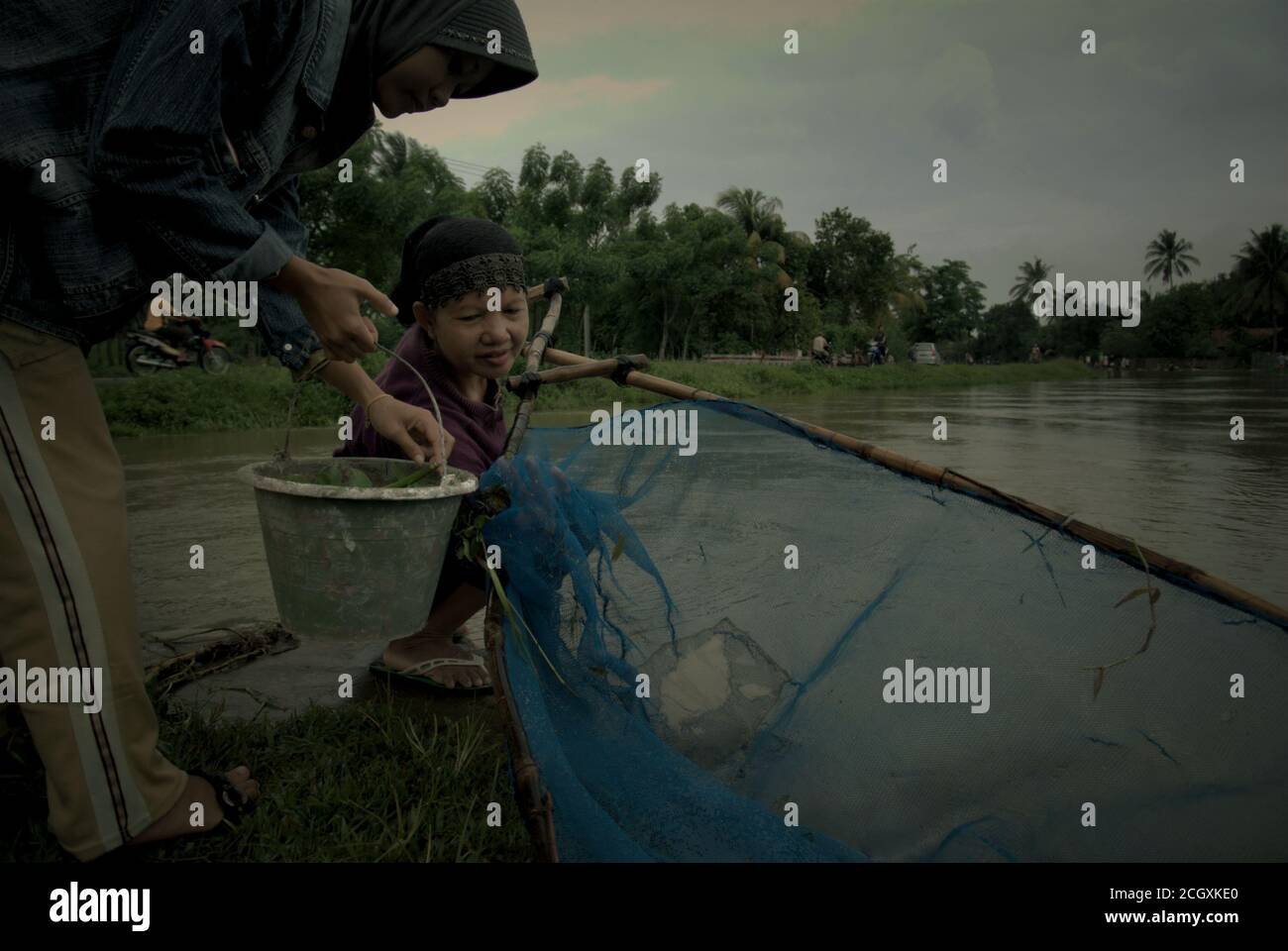 Une femme qui manipule la chathnet tandis que son ami porte le seau en plastique contenant la capture comme ils pêchent sur un canal d'irrigation à Karawang, Indonésie. Banque D'Images