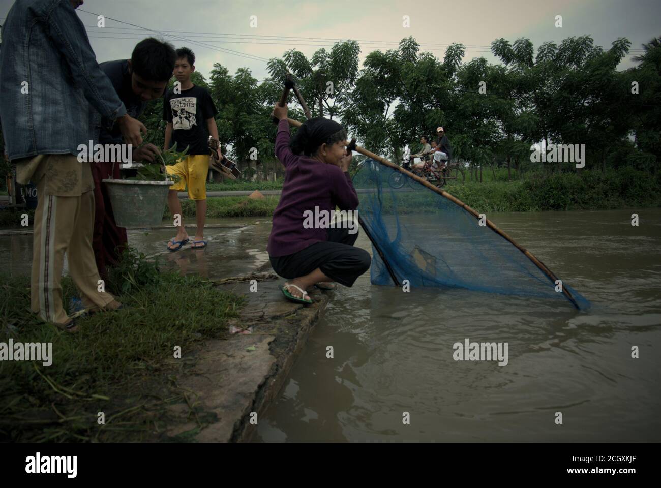 Une femme qui manipule la chathnet tandis que son ami porte le seau en plastique contenant la capture comme ils pêchent sur un canal d'irrigation de bord de route dans Karawang regency, province de Java Ouest, Indonésie. Banque D'Images