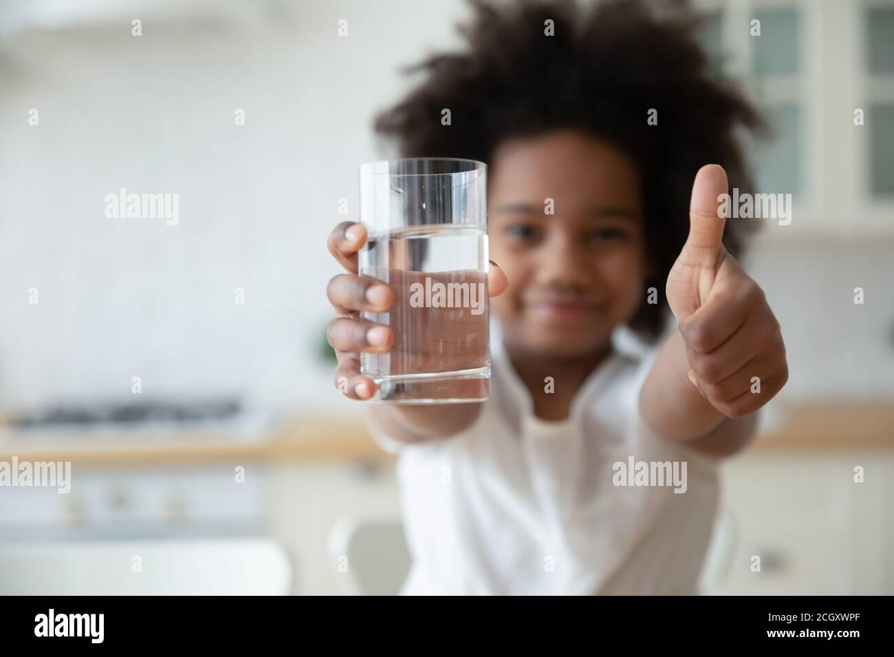 Biracial fille tenant un verre d'eau, montrant les pouces vers le haut geste. Banque D'Images