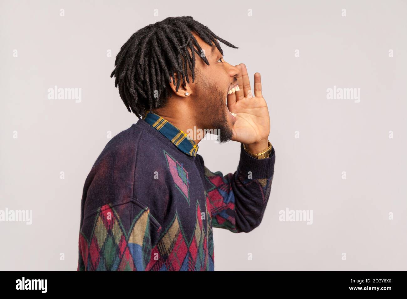 Vue latérale Africain avec des dreadlocks élégants criant bruyamment, annonce d'informations importantes, phobie. Prise de vue en studio isolée sur fond gris Banque D'Images