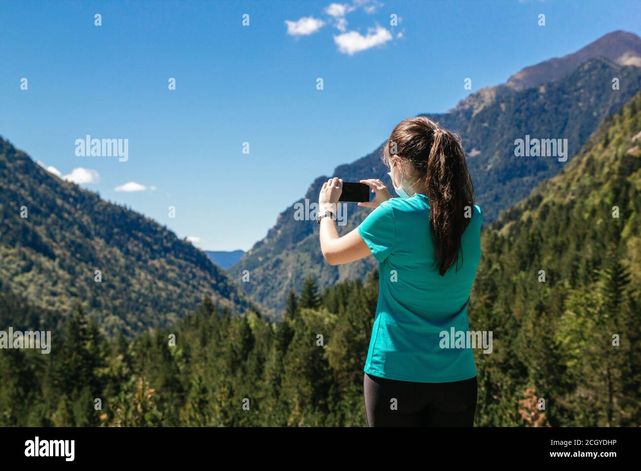 Photo d'une jeune femme avec masque de prise une photo d'un magnifique paysage de montagne avec son smartphone Banque D'Images