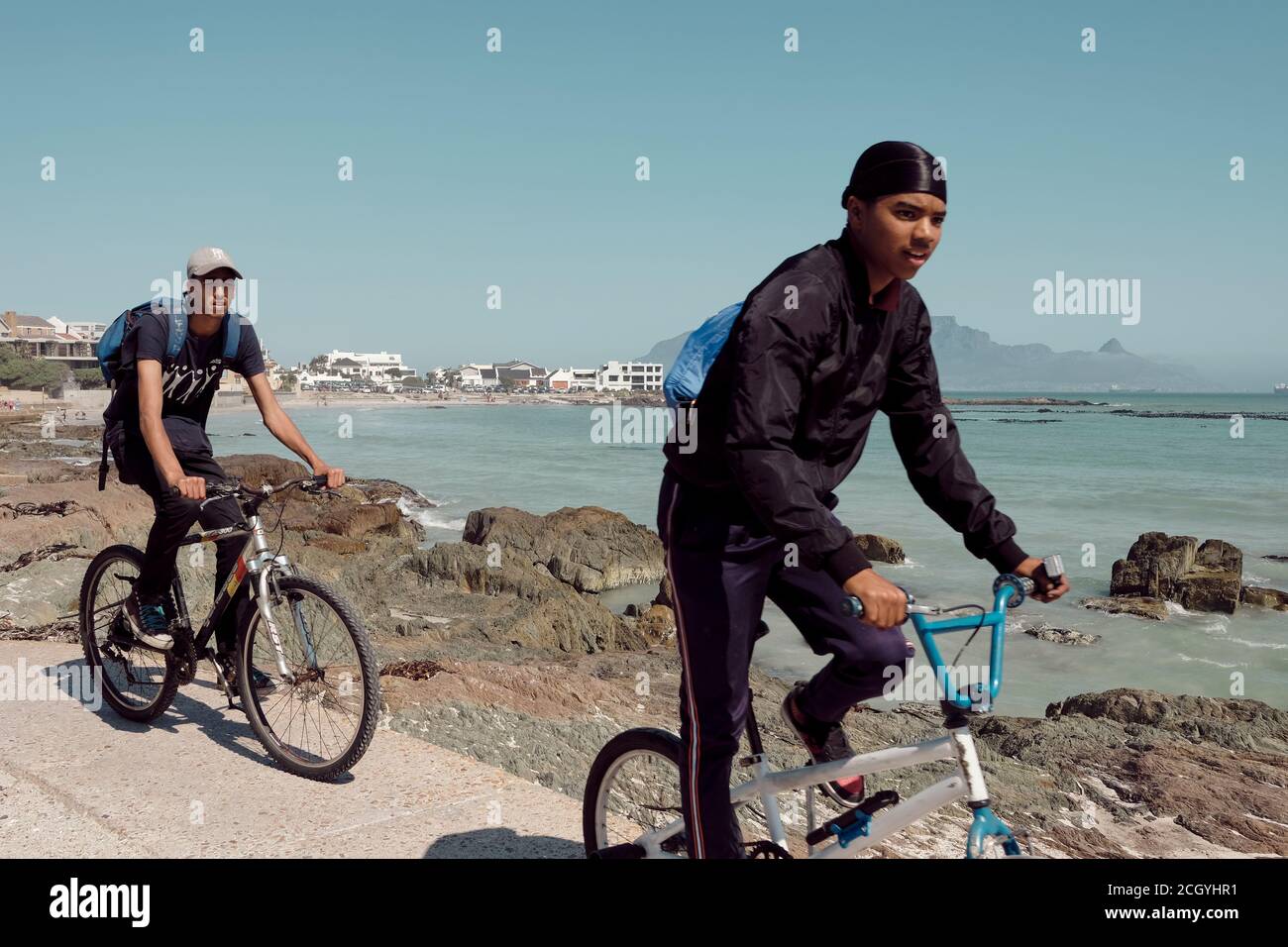 Les jeunes qui voyagent à vélo sur la très populaire plage de Bloubergstrand au Cap, en Afrique du Sud. Montagne de table en arrière-plan. Banque D'Images