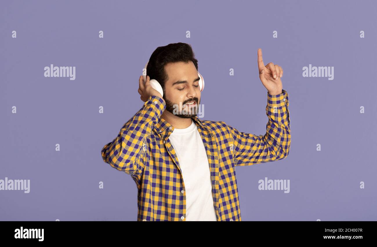 Amant musical indien du millénaire appréciant ses chansons préférées dans un casque sur fond violet Banque D'Images