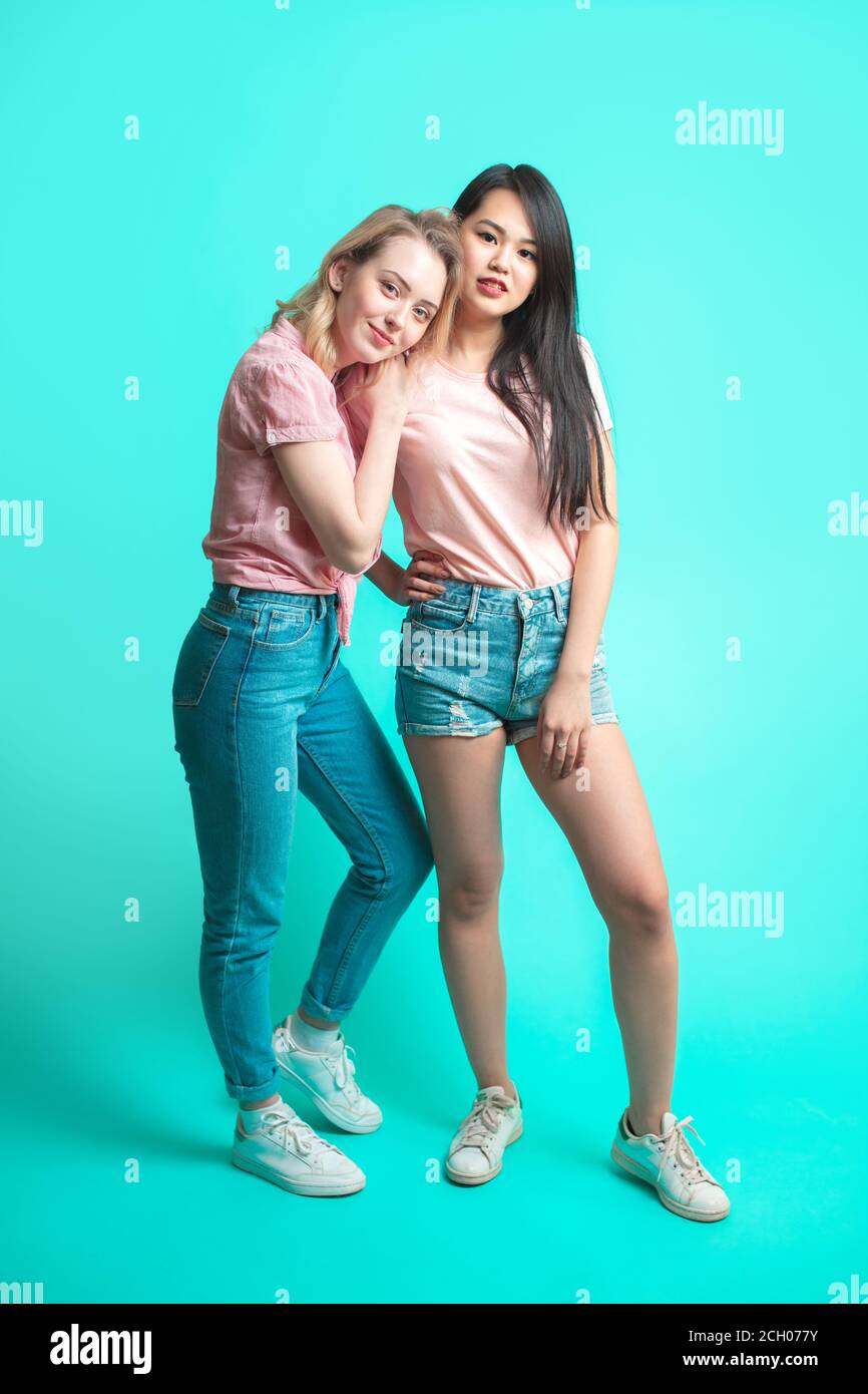 Portrait of young différentes nationalités teenage girlfriends, caucasian woman et Asian Woman - hagging, isolé sur fond bleu. Woma européenne Banque D'Images