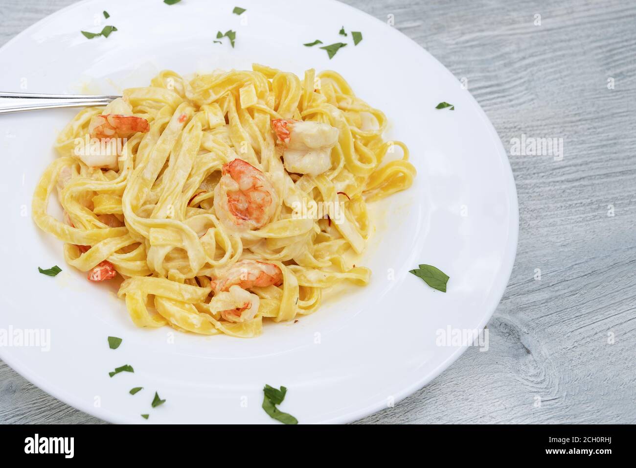 Pâtes tagliatelles aux crevettes et sauce safran dans une assiette blanche sur une table en bois gris, espace de copie, foyer sélectionné, champ étroit Banque D'Images