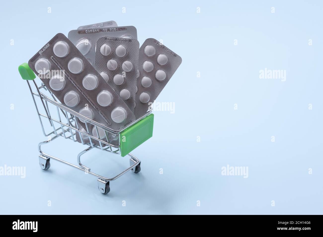 Chariot d'épicerie avec pilules, concept d'achat de pharmacie. Pilules dans le petit chariot d'épicerie sur fond bleu. copyspace Banque D'Images