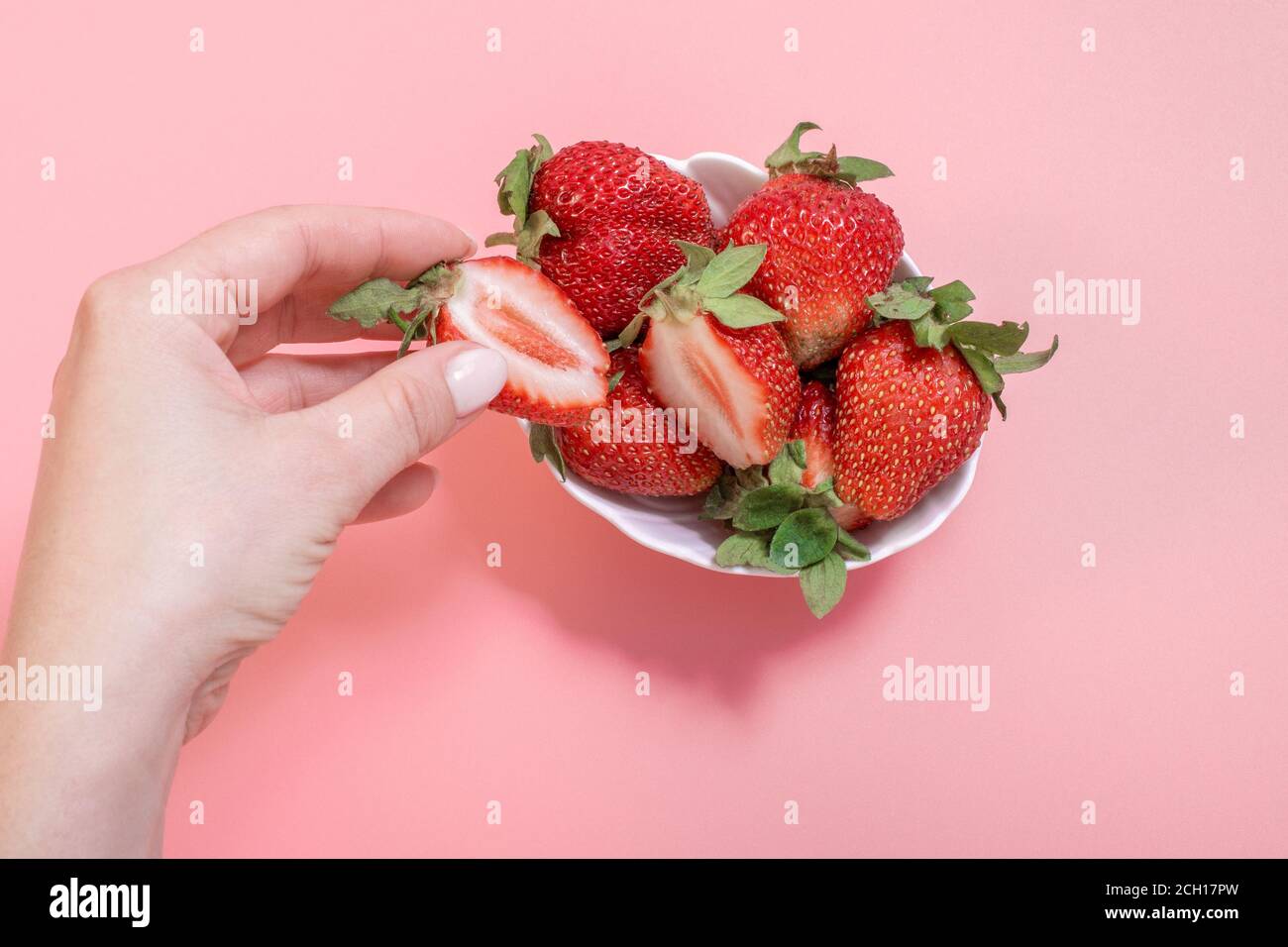 La main d'une femme prend des fraises dans un bol. Main de femme tenant la fraise sur fond rose, assiette de fraises. Concept de saine alimentation d'été. Banque D'Images