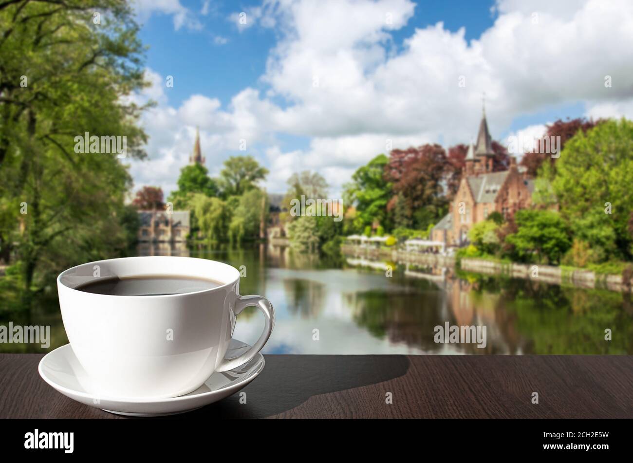 Une tasse de café sur la table avec vue sur le parc vert avec le lac Minnewater et le petit château de Bruges pendant la journée ensoleillée au printemps, Belgique Banque D'Images Une tasse de café sur la table avec vue sur le parc vert avec le lac Minnewater et le petit château de Bruges pendant la journée ensoleillée au printemps, Belgique Banque D'Images