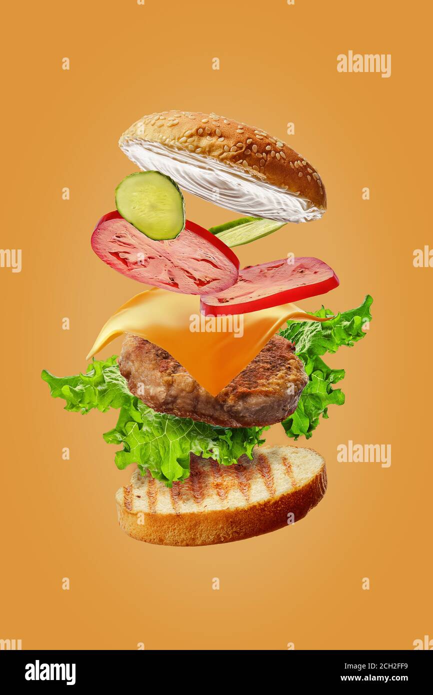 Hamburger avec ingrédients volants isolés sur fond orange Banque D'Images