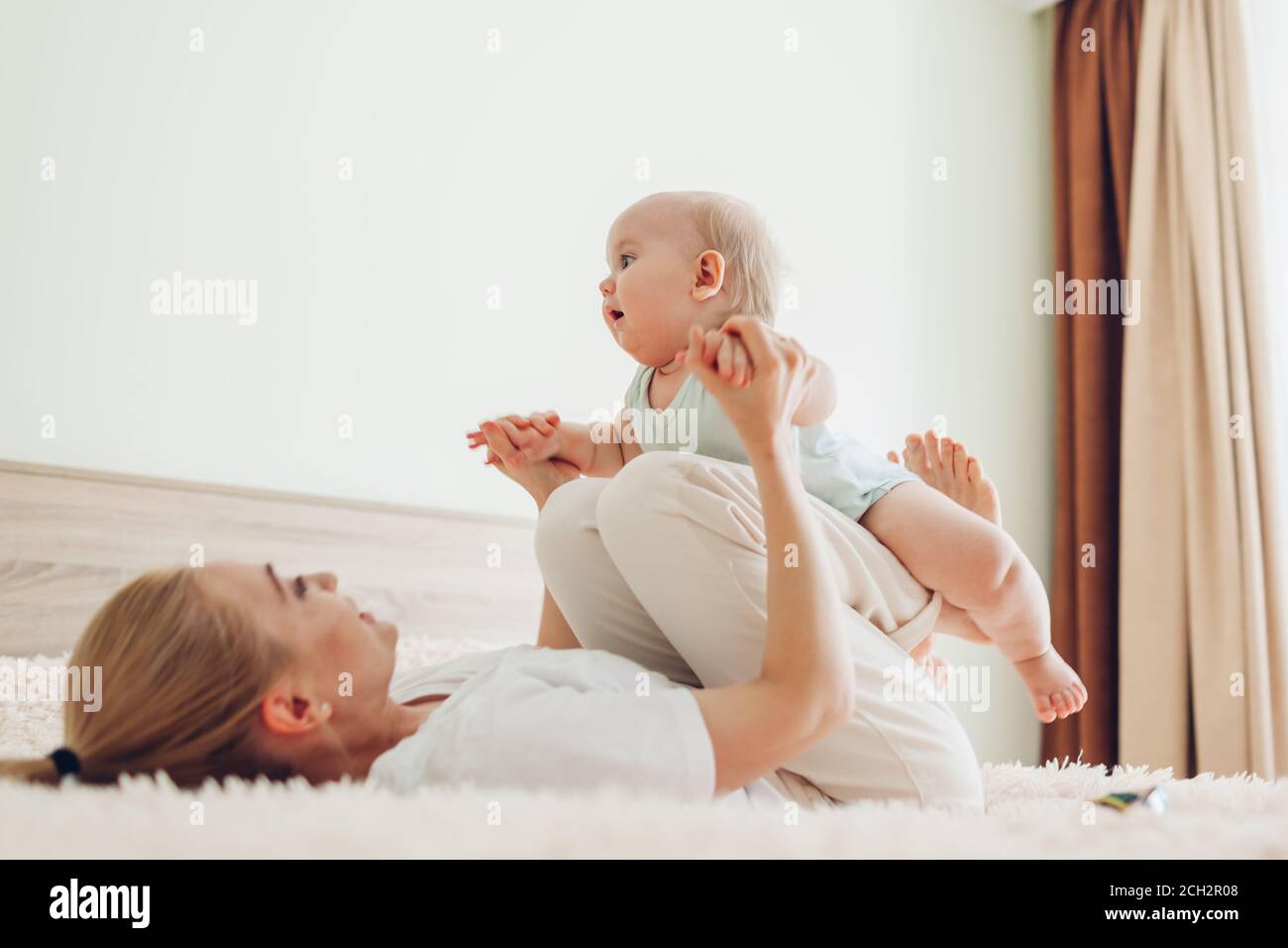 Jeune mère jouant avec son bébé fils nouveau-né à la maison. Famille s'amusant allongé sur le lit dans la chambre Banque D'Images