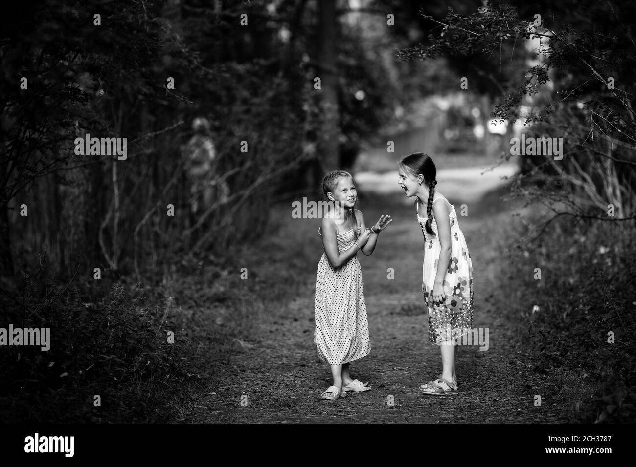 De jolies petites filles, qui parlent avec enthousiasme dans le parc. Photo en noir et blanc. Banque D'Images