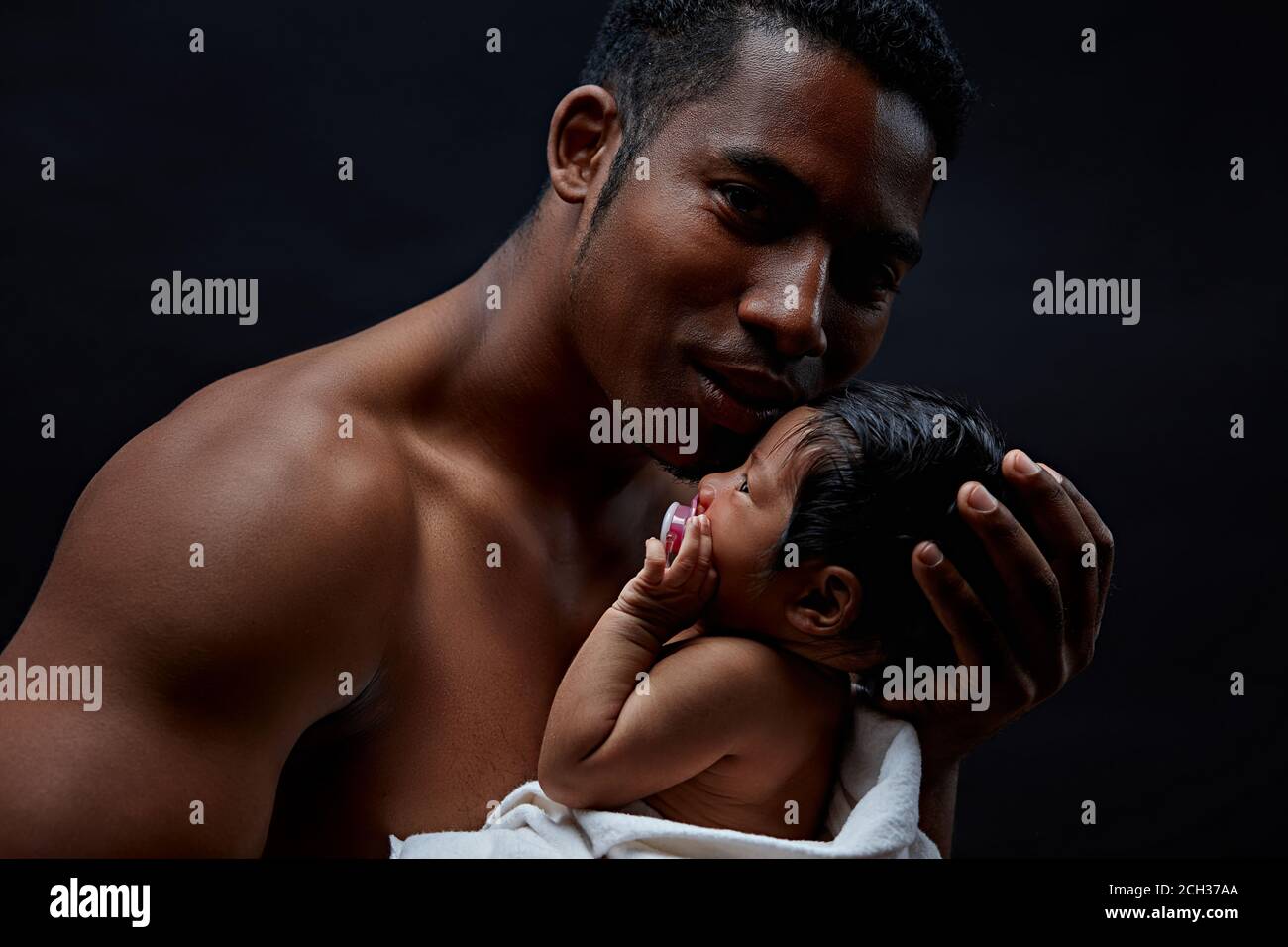 un beau père brutal embrasse son bébé, isolé sur fond noir. Banque D'Images