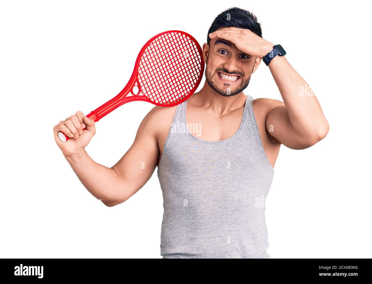 Jeune homme beau tenant une raquette de tennis stressé et frustré avec la main sur la tête, surpris et fâché visage Banque D'Images
