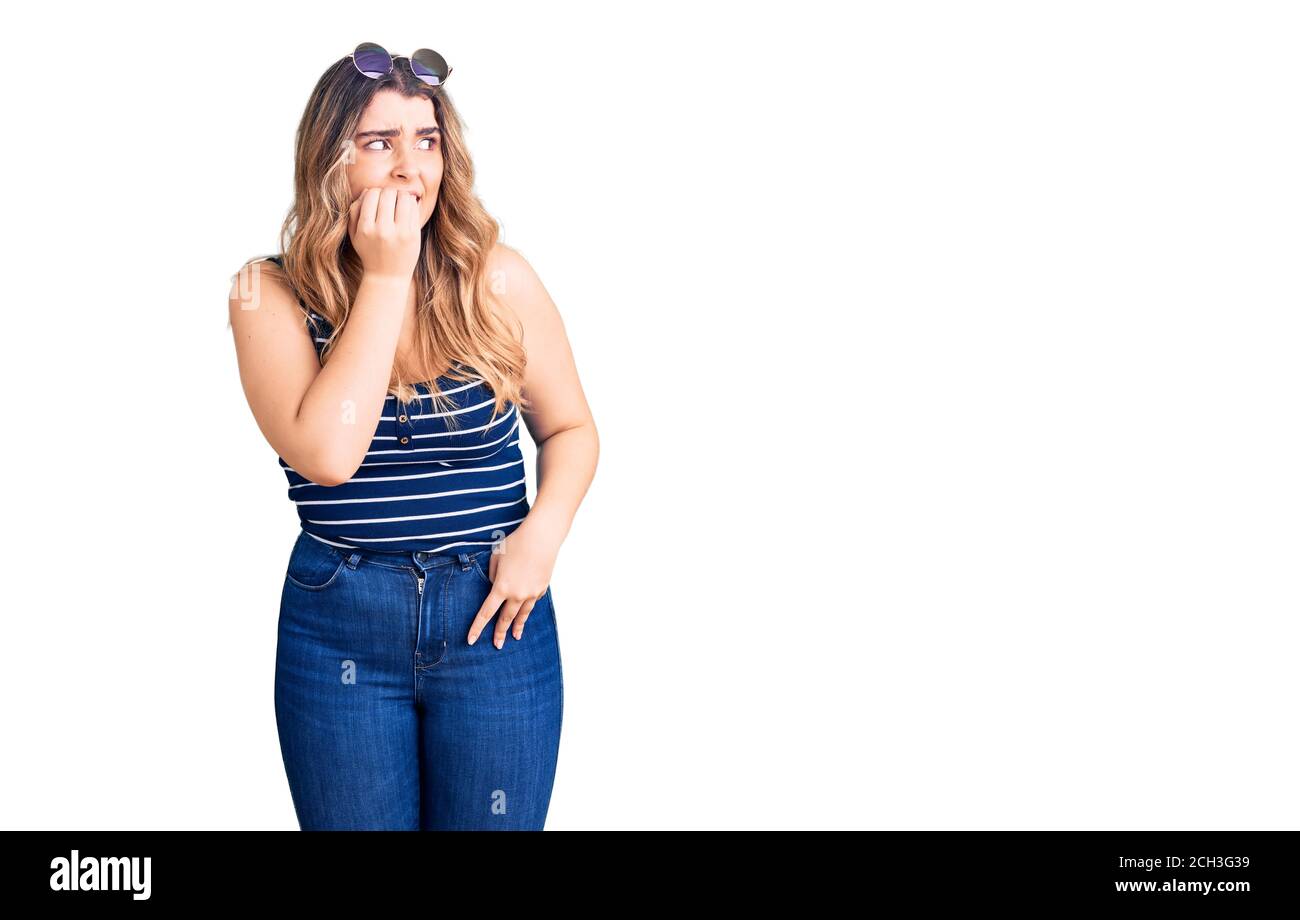 Jeune femme caucasienne portant des vêtements décontractés et des lunettes de soleil ayant l'air stressée et nerveuse avec les mains sur la bouche piquant les ongles. Banque D'Images