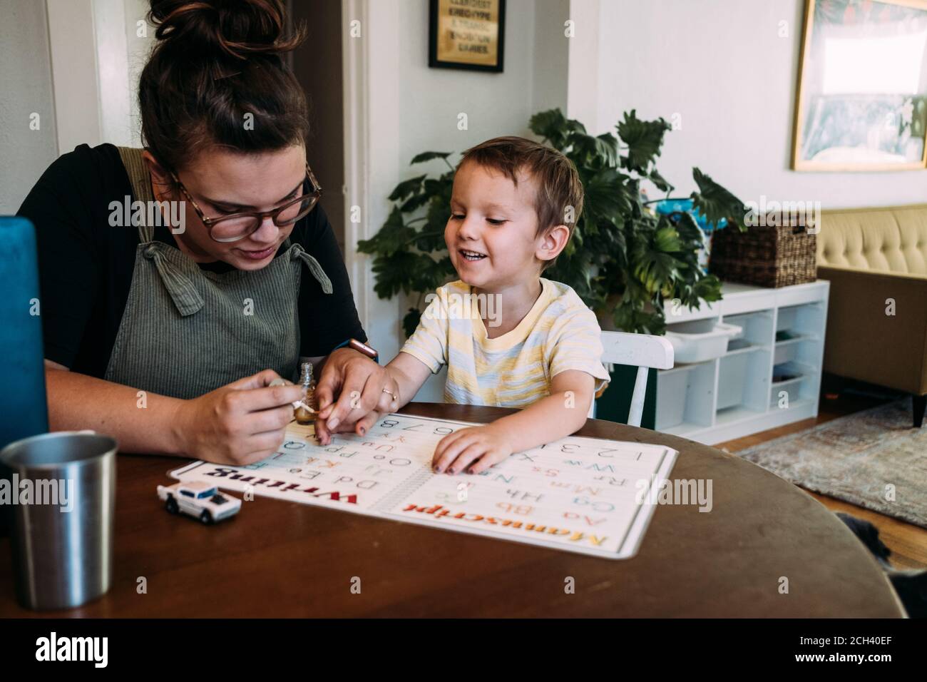 Maman peignant les ongles du doigt du fils souriant à la table de cuisine Banque D'Images